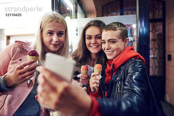Drei junge Frauen mit Eiswaffeln nehmen Smartphone-Selfie mit auf die Straße