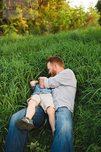 Vater kitzelt Sohn im hohen Gras