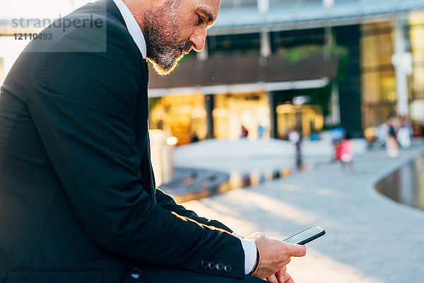 Reifer Geschäftsmann sitzt im Freien und benutzt ein Smartphone