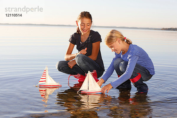 Zwei junge Mädchen treiben Spielzeugboote auf dem Wasser