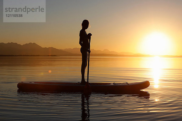 Junge Mädchen paddeln auf dem Wasser  bei Sonnenuntergang