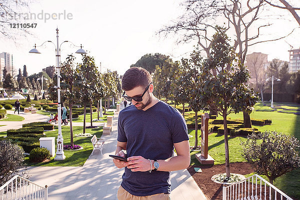 Mann mit Sonnenbrille auf der Parktreppe mit Blick auf Smartphone