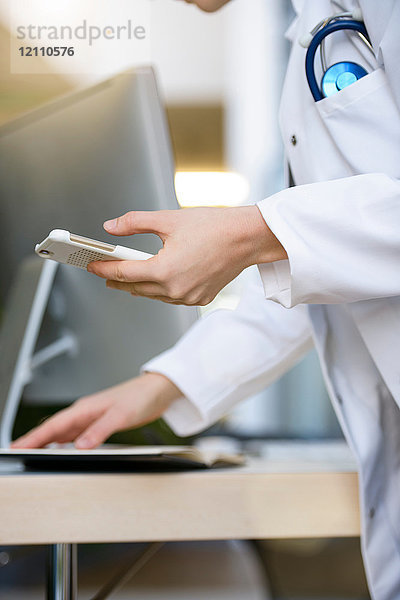 Ärztin  die ein Smartphone in der Hand hält und einen Laptop benutzt  mittlerer Abschnitt