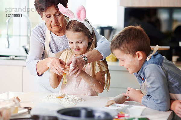Großmutter hilft Mädchen beim Osterbacken an der Küchentheke