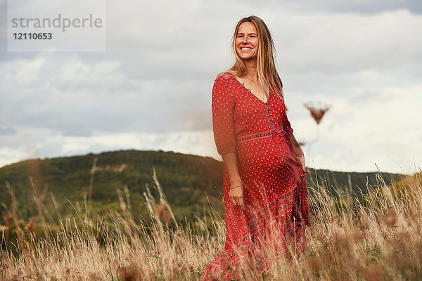 Porträt einer glücklichen schwangeren Frau in rotem Kleid am Hang