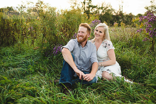 Ehepaar sitzt im hohen Gras und schaut lächelnd weg