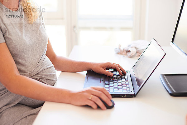 Schnappschuss einer schwangeren jungen Frau am Schreibtisch beim Tippen am Laptop