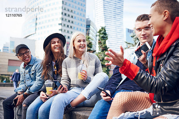 Fünf junge erwachsene Freunde sitzen auf einer Mauer und unterhalten sich in der Stadt
