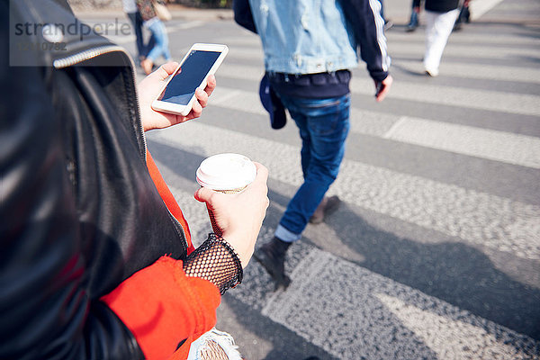 Person auf dem Fussgängerstreifen mit Kaffee und Smartphone