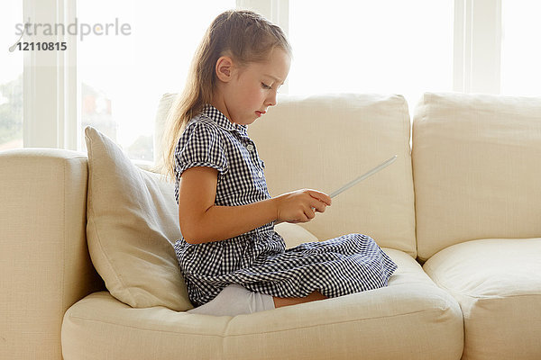 Junges Mädchen  auf Sofa sitzend  mit digitalem Tablett