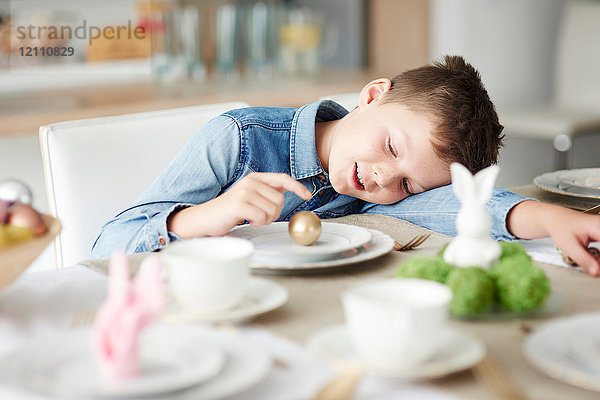 Junge am Esstisch  der mit goldenem Osterei auf dem Teller spielt