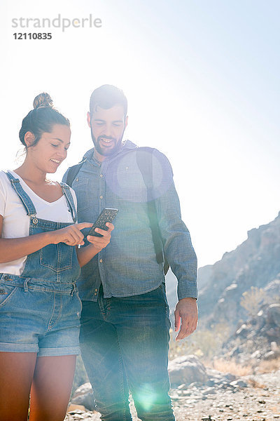 Junges Wanderpaar betrachtet Smartphone im sonnenbeschienenen Tal  Las Palmas  Kanarische Inseln  Spanien