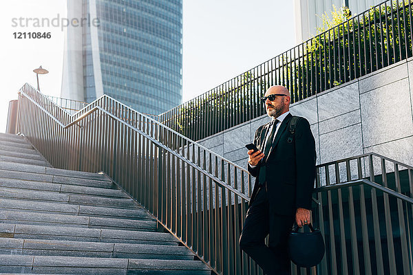 Älterer Geschäftsmann auf Stufen stehend  mit Smartphone  niedriger Blickwinkel