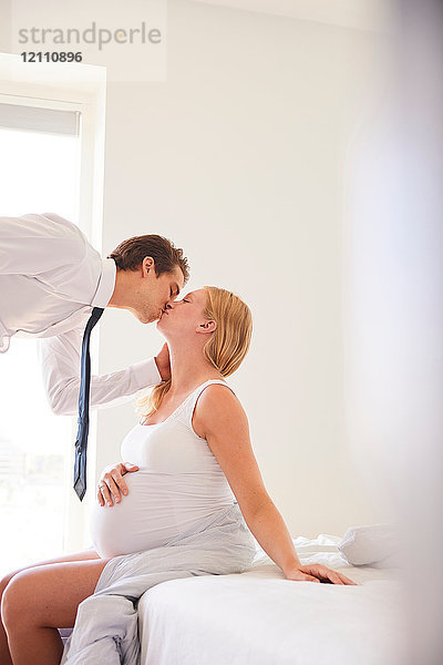 Schwangere Frau küsst Geschäftsmann-Ehemann im Schlafzimmer