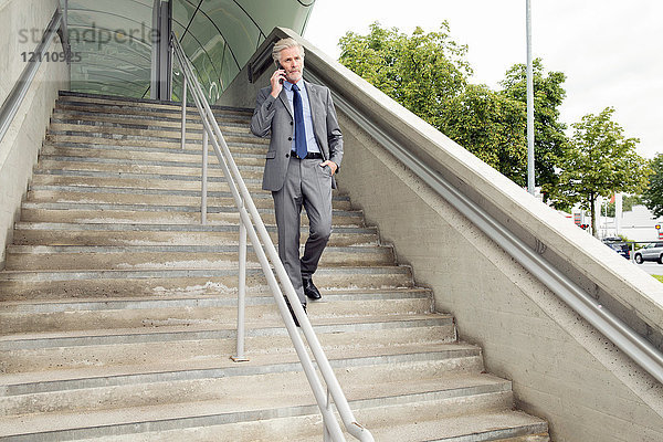 Geschäftsmann geht die Treppe hinunter und telefoniert mit einem Smartphone