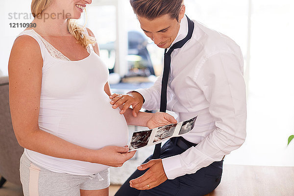 Schwangeres Paar betrachtet Ultraschallbilder im Wohnzimmer