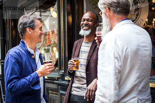 Drei reife Männer  die vor der Kneipe stehen  Biergläser halten und lachen