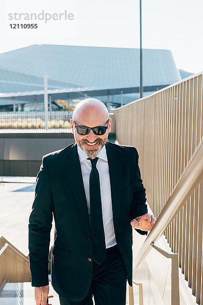 Porträt eines reifen Geschäftsmannes im Freien  der eine Treppe hinaufgeht und eine Sonnenbrille trägt