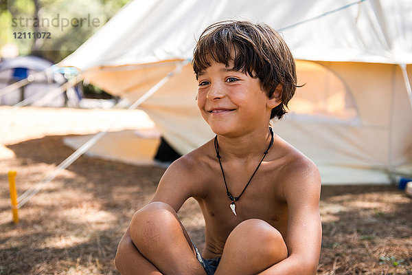 Glücklicher Junge mit nackter Brust auf dem Campingplatz sitzend