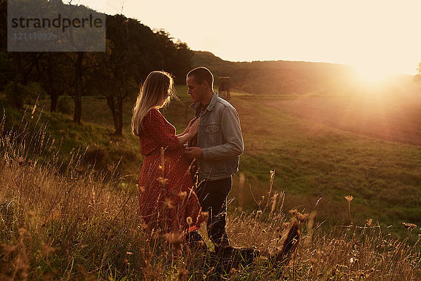 Romantisches schwangeres Paar im mittleren Erwachsenenalter von Angesicht zu Angesicht am Hang bei Sonnenuntergang