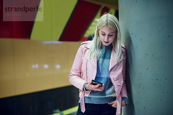 Junge Frau wartet in U-Bahn-Station und schaut auf Smartphone