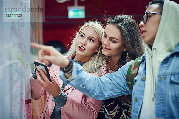 Drei junge erwachsene Freunde zeigen in der U-Bahn-Station auf eine Karte