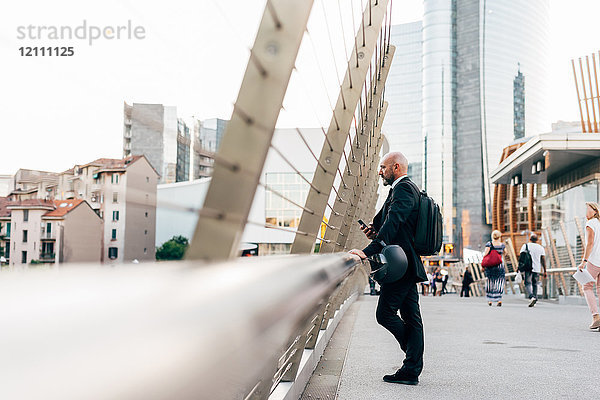 Reifer Geschäftsmann steht auf der Brücke  schaut auf die Aussicht  hält Smartphone