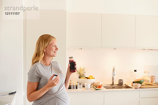 Schwangere junge Frau in der Küche mit einer Flasche Fruchtsaft