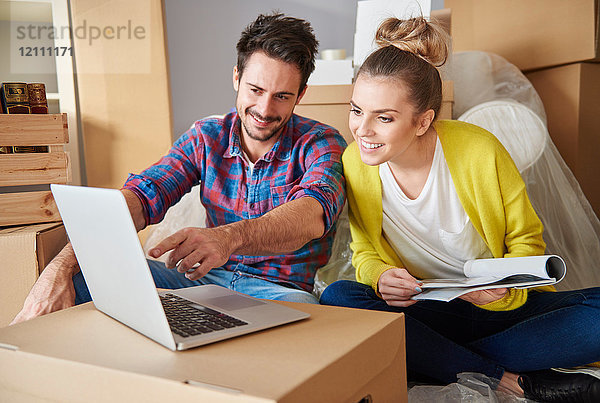 Junges Paar zu Hause  umgeben von Pappkartons  schaut auf den Laptop