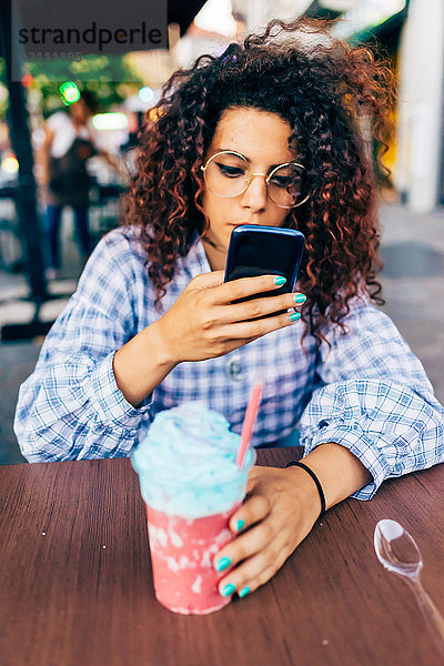Frau benutzt Mobiltelefon  während sie ein eiskaltes Getränk genießt