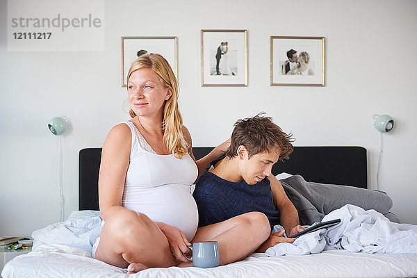 Mann und schwangere Freundin entspannen sich mit Hilfe eines digitalen Tablets im Bett