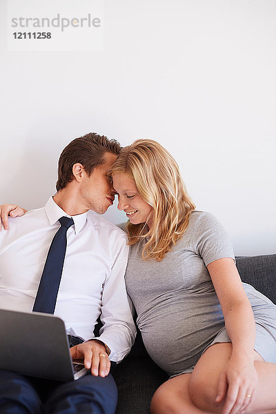 Romantischer Mann flüstert seiner schwangeren Freundin auf dem Sofa zu