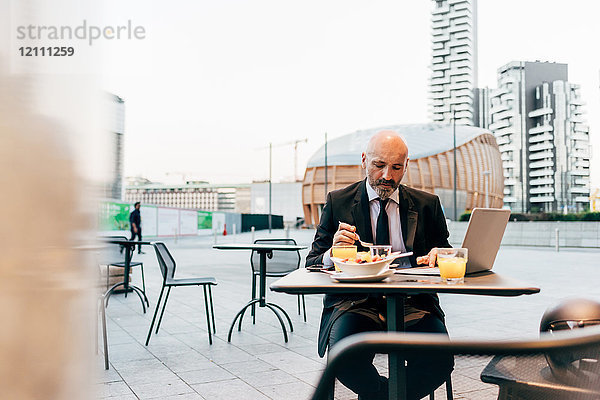 Ein reifer Geschäftsmann sitzt draußen im Café und benutzt einen Laptop