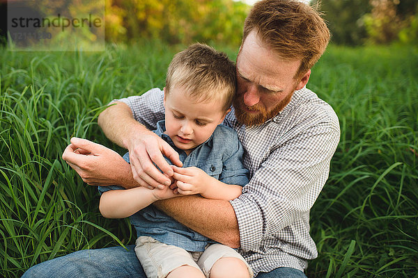 Vater und Sohn sitzen im hohen Gras und erforschen die Natur