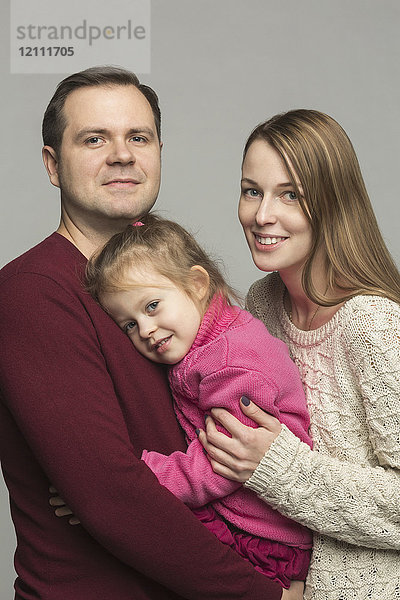 Porträt glücklicher Eltern mit Tochter vor grauem Hintergrund