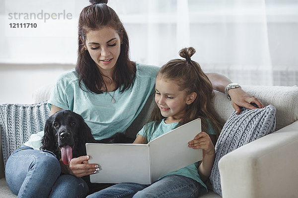 Mädchen-Lesebuch von Mutter und Hund auf dem Sofa zu Hause