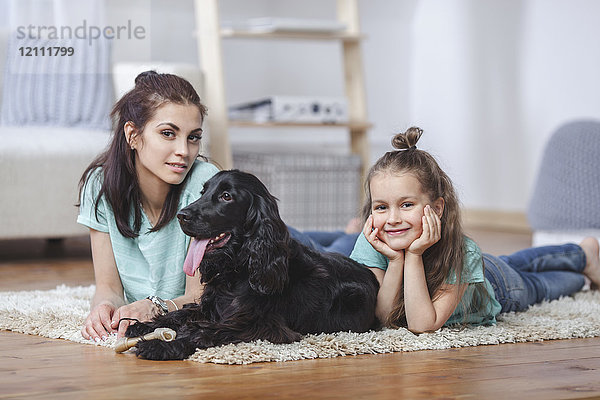 Porträt von Mutter und Tochter liegend mit Hund auf Teppich zu Hause