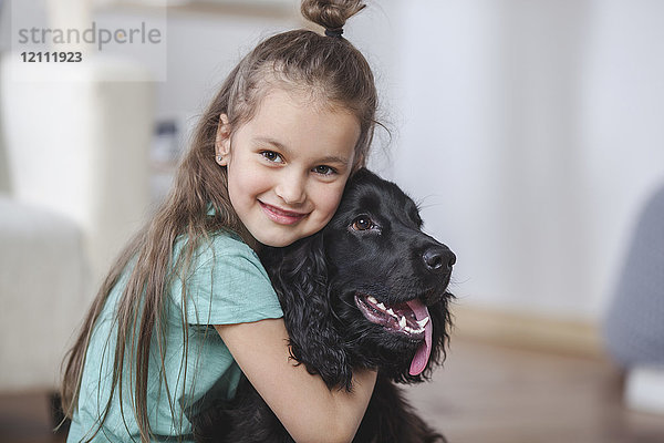 Porträt eines lächelnden Mädchens  das Cocker Spaniel zu Hause umarmt.