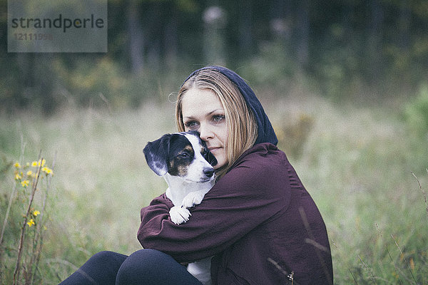 Nachdenkliche Frau umarmt Hund beim Sitzen auf grasbewachsenem Feld