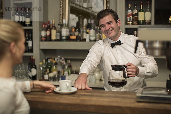 Lächelnder Barkeeper bei der Zubereitung einer Tasse Kaffee für die Frau