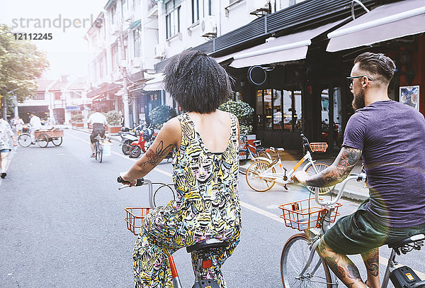 Multi-ethnisches Hipster-Paar radelt entlang der Stadtstraße  Shanghai Französische Konzession  Shanghai  China