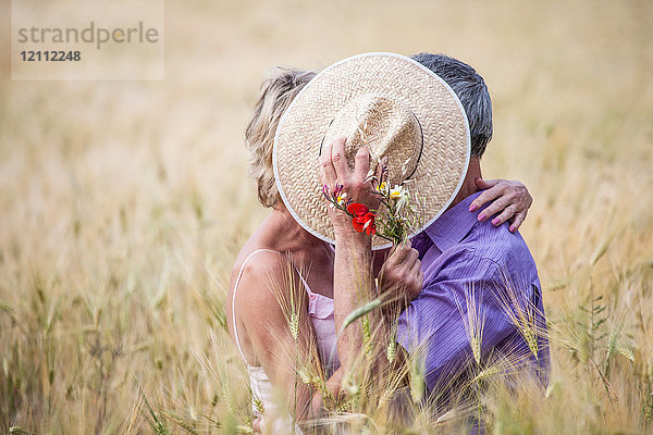 Paar auf dem Feld im hohen Gras  das Gesichter mit Strohhut bedeckt
