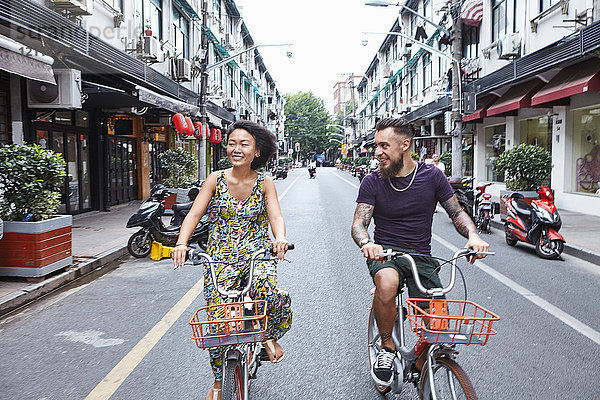 Multi-ethnisches Hipster-Paar radelt entlang der Stadtstraße  Shanghai Französische Konzession  Shanghai  China