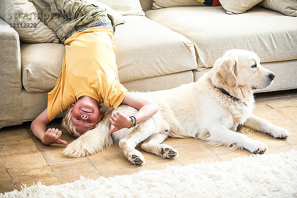 Junge kopfüber auf dem Sofa liegend mit Hund