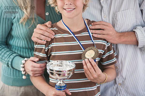 Schrägansicht eines Jungen  der stolz Trophäe und Medaille hält