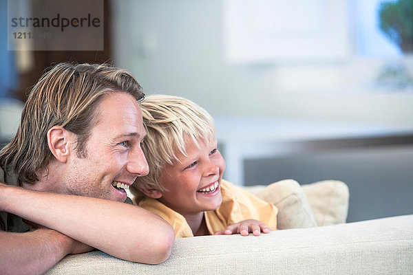 Vater und Sohn entspannen sich auf dem Sofa und schauen lächelnd weg