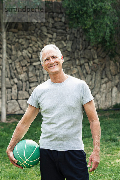 Porträt eines Mannes  der einen Basketball hält und lächelnd in die Kamera schaut