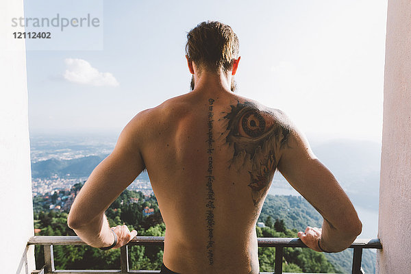 Tätowierter junger Mann schaut von Aussichtsplattform hinunter  Comer See  Lombardei  Italien