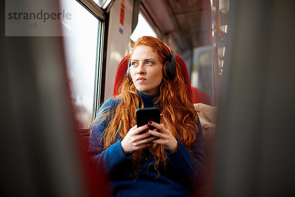 Frau im Zug  die mit Kopfhörern Musik auf Mobiltelefonen hört  London