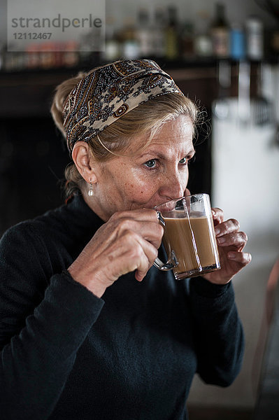 Blonde ältere Frau mit blonden Haaren trinkt Kaffee in der Küche